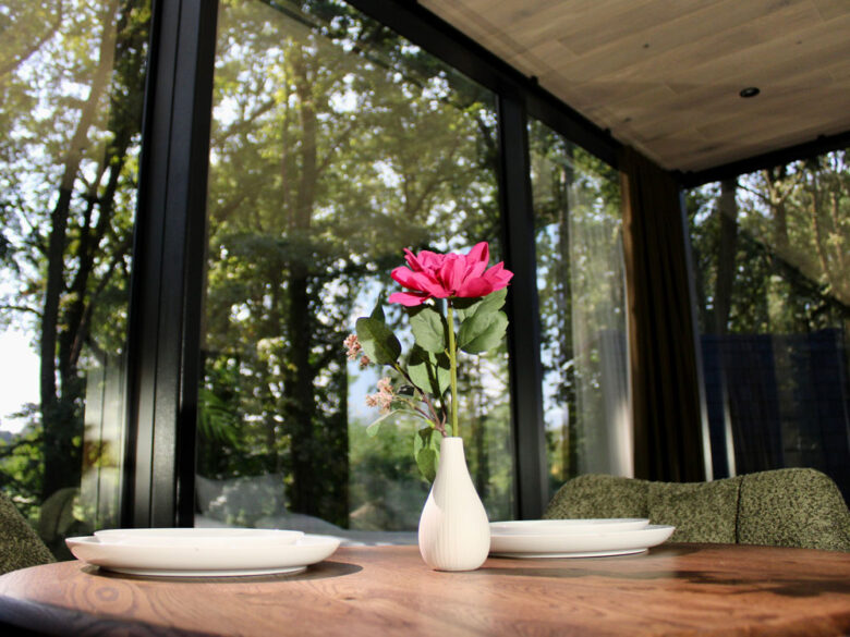 Gedeckter Esstisch mit Blumenvase im Spiegelhaus mit Panoramafenster zum Wald