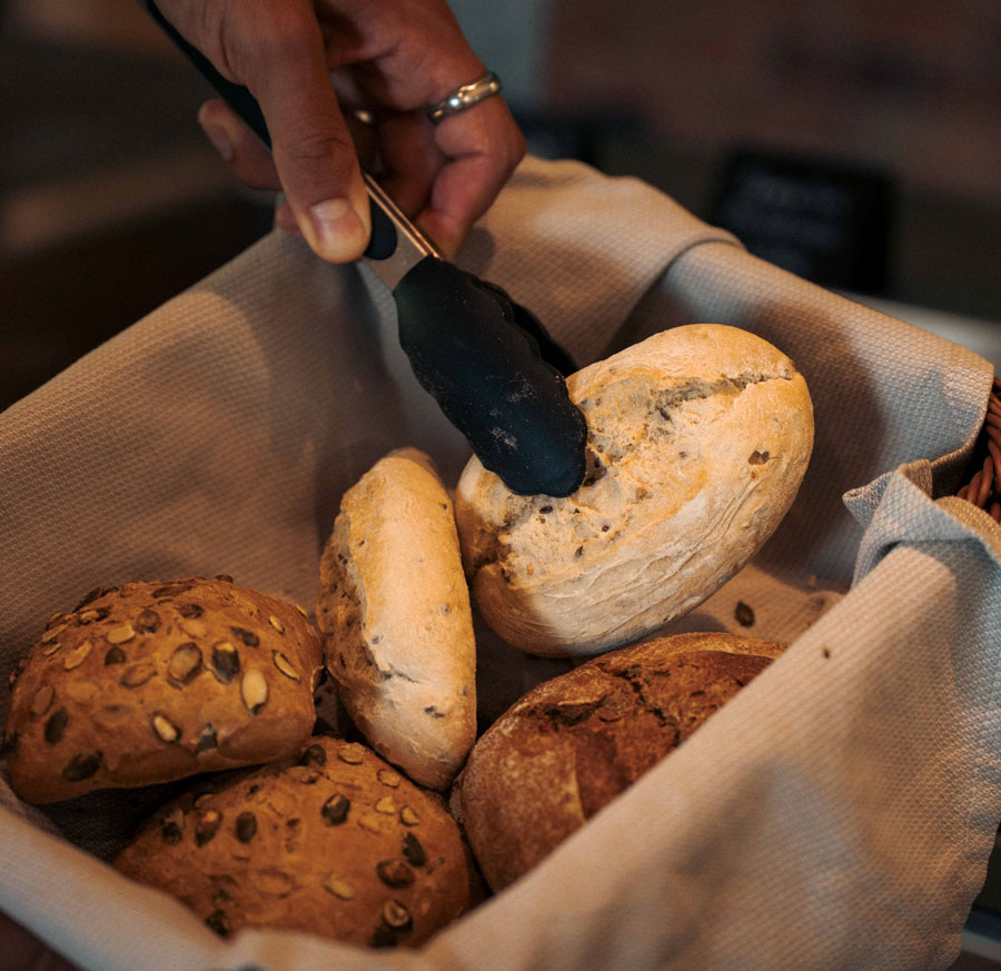 Hand entnimmt frische Brötchen mit der Zange aus dem Frühstückskorb