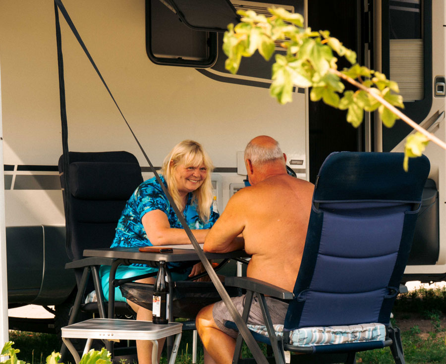 Paar sitzt plaudernd am Campingtisch vor dem Wohnwagen beim Camping in Oranienburg