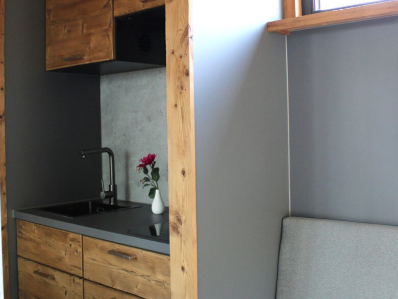 Küchenzeile im SpaCube mit Holzfronten, schwarzer Spüle und angrenzendem Sofa