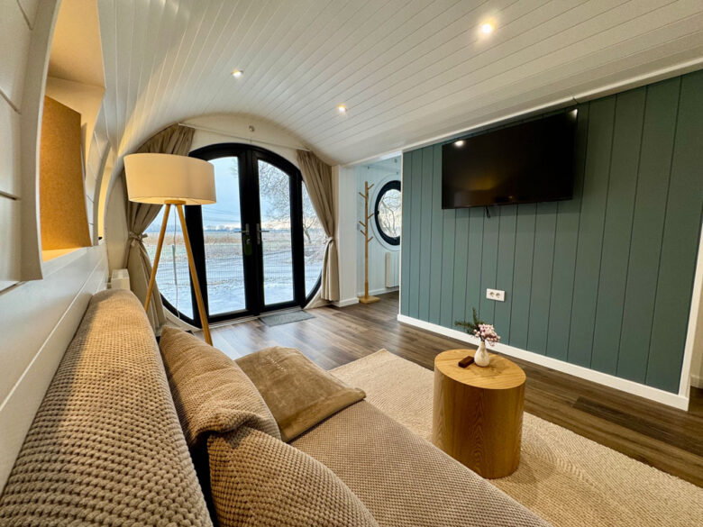 Wohnbereich der PodLodge mit Strick-Sofa, Wand-TV und Panoramatür, tiny house für Familien