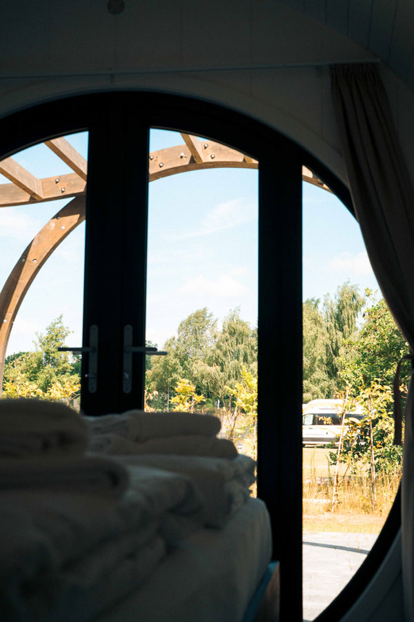Blick durch die runde Fenstertür des tiny house in Brandenburg auf Wohnmobil und Bäume