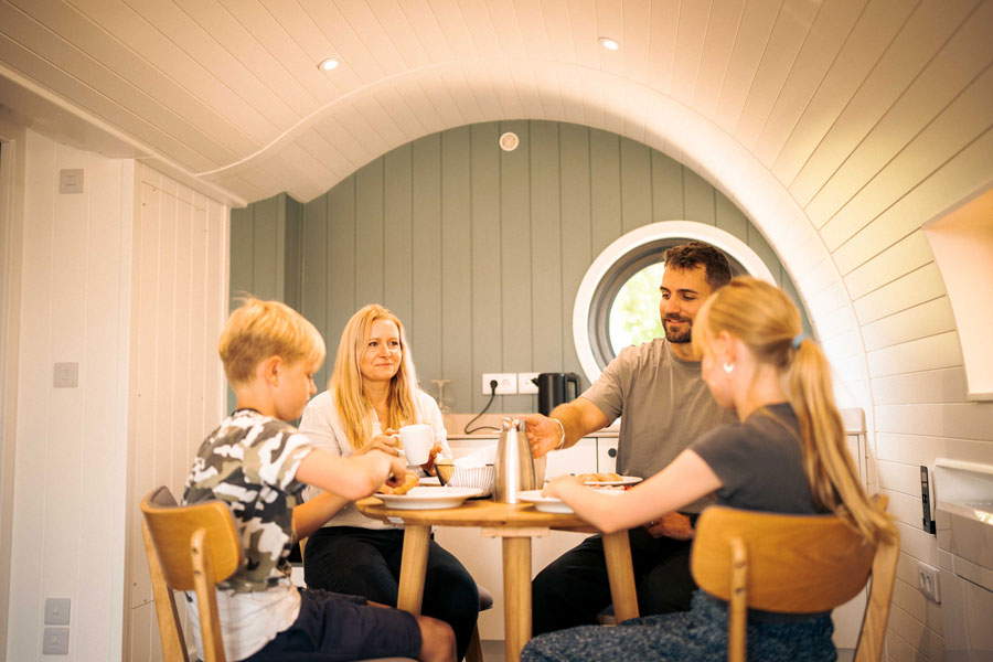 Familie beim Frühstück im tiny house mit Bullaugenfenster, gemütlicher Essbereich mit Küche
