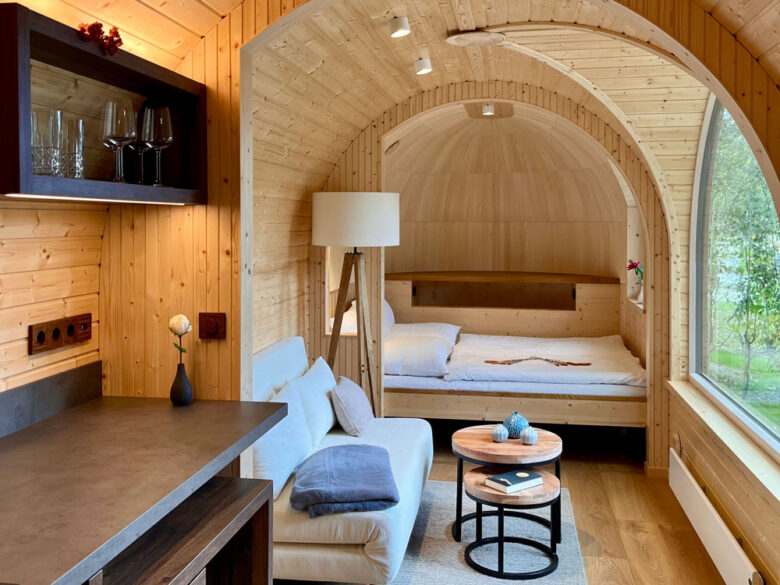 Gemütlicher Innenraum des Iglu mit Sofa, Bett in der Holzkuppel und rundem Fenster