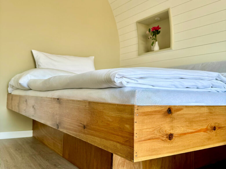 Gemütlicher Schlafbereich der NestLodge mit Holzbett und frischer Bettwäsche, übernachten mit Hotelkomfort