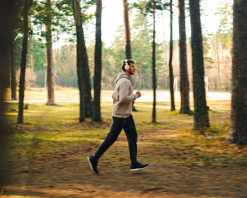 Mann joggt mit Kopfhörern durch den herbstlichen Kiefernwald am Resort