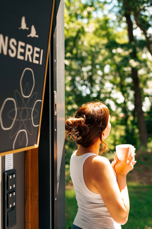 Junge Frau genießt ihren Morgenkaffee neben der Infotafel im grünen Waldresort