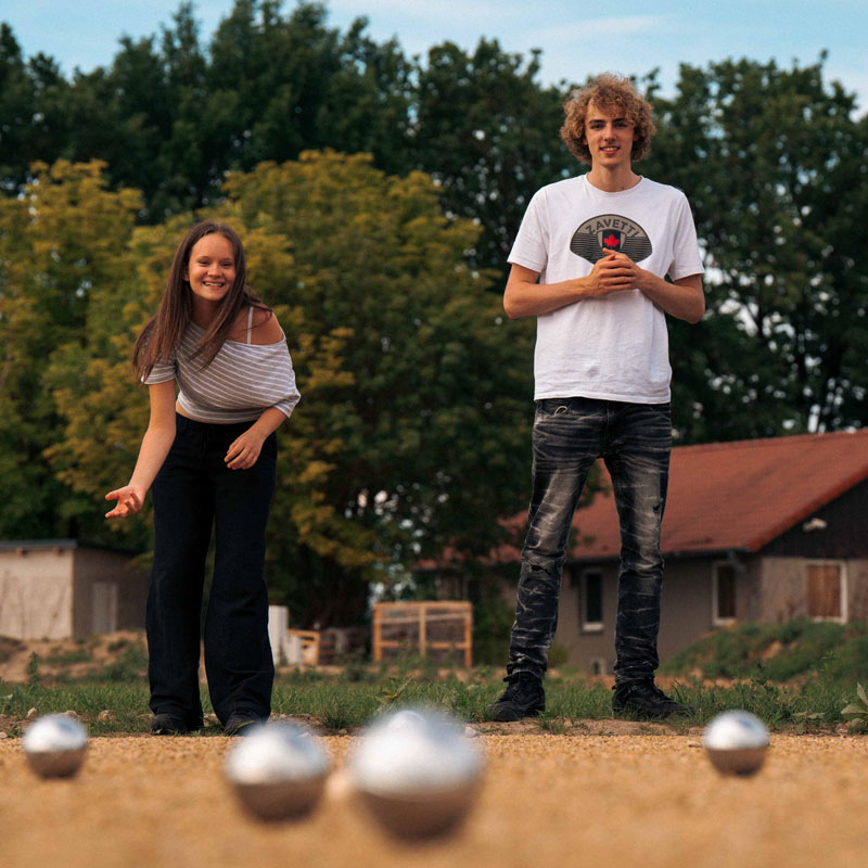 Zwei junge Gäste spielen Boule auf dem Kiesplatz im Naturresort CARAVANSEREI