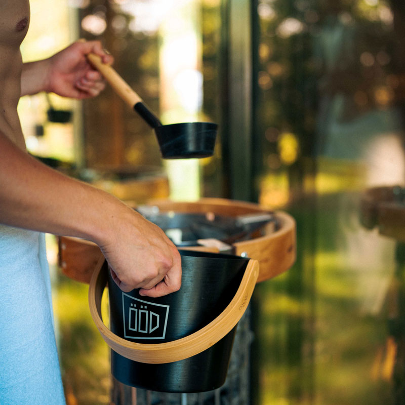 Gast greift Saunakübel und Aufgusskelle an der Tiny Spa mit Sauna nahe Berlin