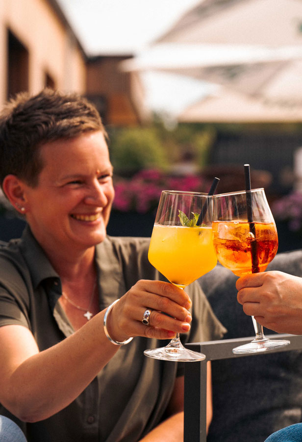 Zwei Frauen stoßen mit Aperitifs auf der sonnigen Terrasse an und genießen den Sommer