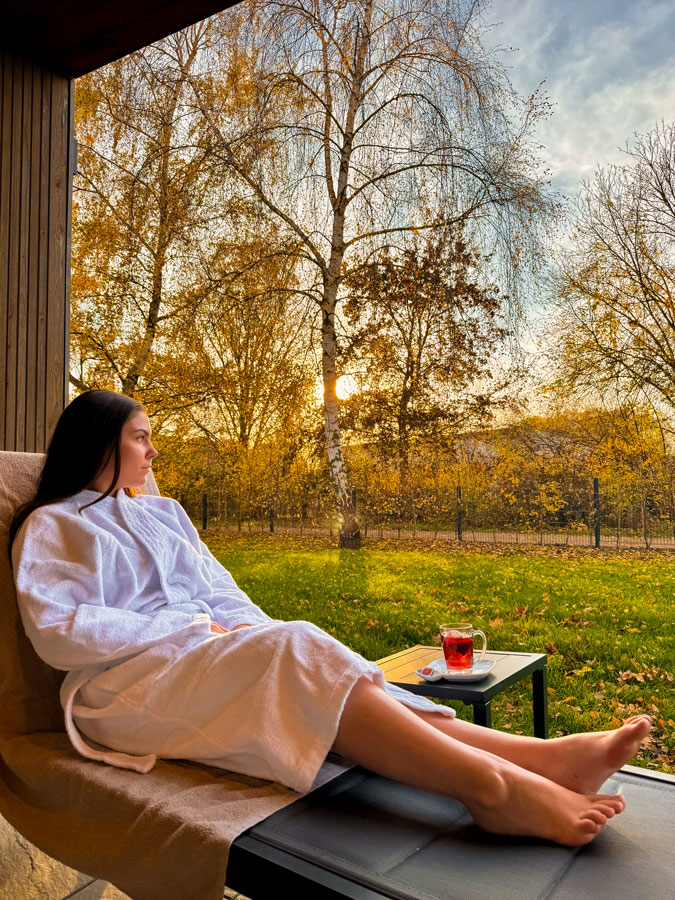 Frau im Bademantel entspannt mit Tee auf der Liege im goldenen Herbstsonnenuntergang