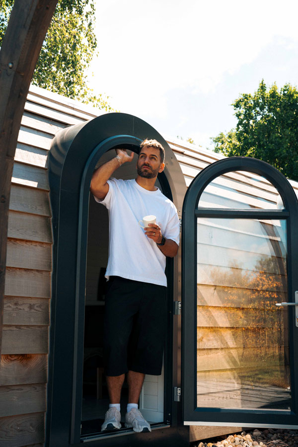 Mann mit Kaffee steht in der runden Tür eines Tiny House im Naturresort bei Berlin