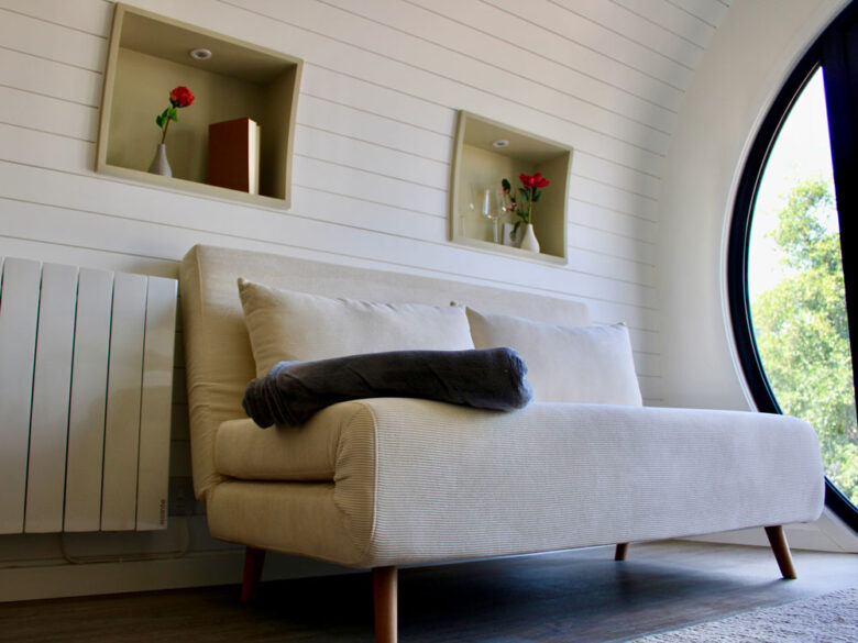 Heller Wohnbereich der NestLodge mit Sofa und rundem Panoramafenster, ferienhaus nahe Berlin