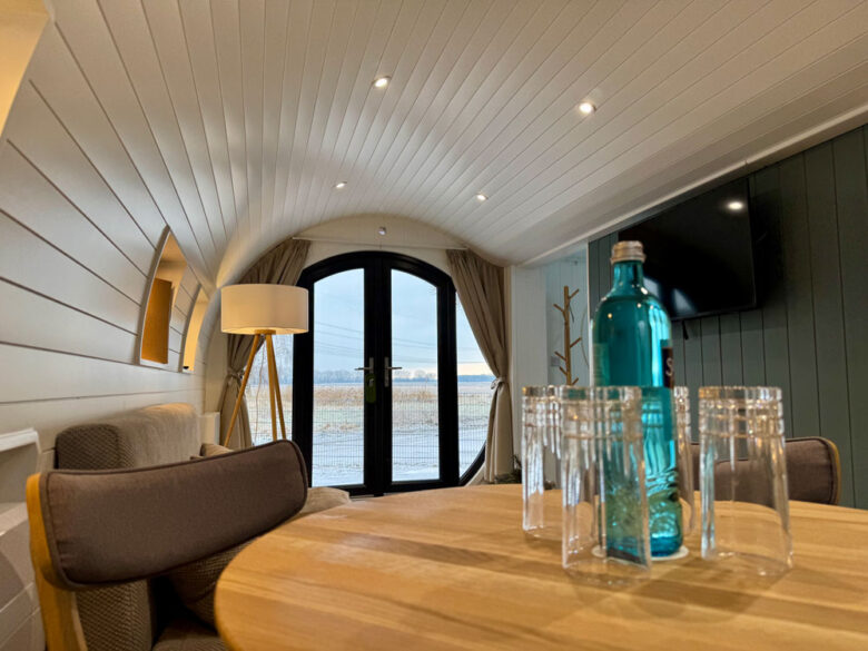 Essbereich der PodLodge mit Holztisch, Gläsern und Terrassentür, glamping in Brandenburg