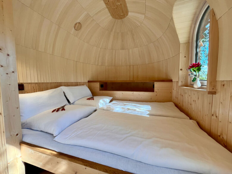 Schlafbereich im IgluPlus mit Doppelbett unter der Holzkuppel und Rundbogenfenster