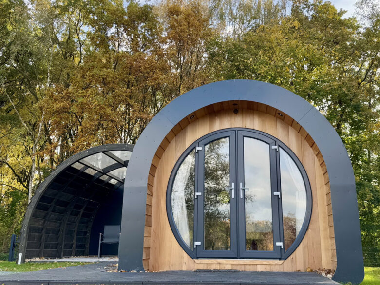NestLodge von vorn mit runder Glastür und überdachter Holzterrasse, tiny house in Brandenburg