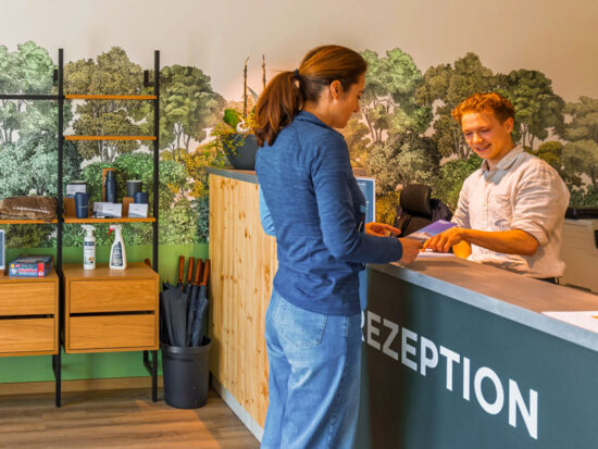 Freundlicher Empfang an der Rezeption der CARAVANSEREI, Gästin erhält ihre Unterlagen beim Check-in