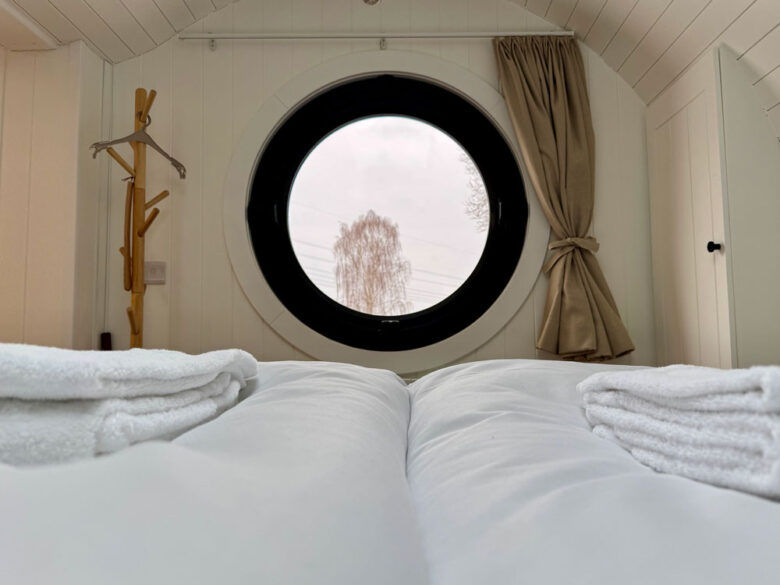 Behaglicher Schlafplatz der PodLodge mit rundem Fenster und Bettwäsche, tiny house in Brandenburg